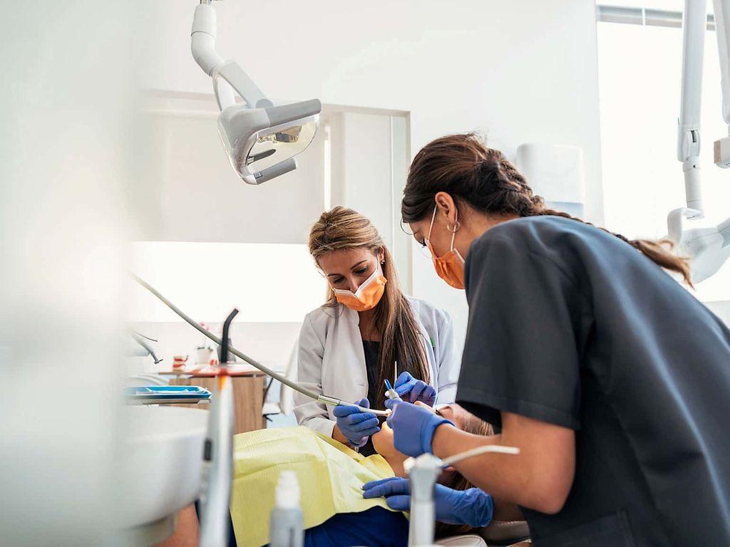 Parodontitis: Frau sitzt auf einem Behandlungsstuhl und wird von einer Zahnärztin behandelt.