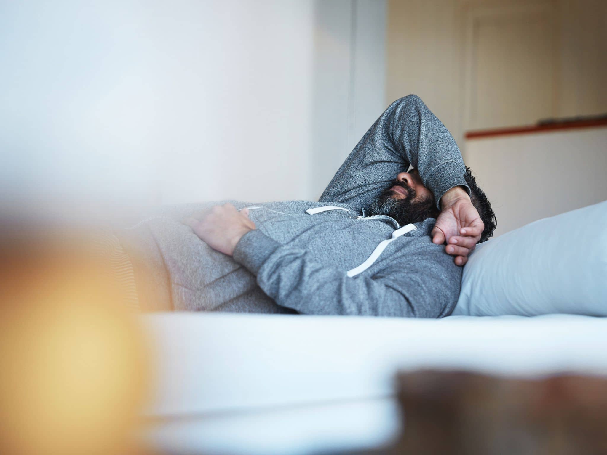 Grippe: Man liegt im Bett und hält sich Hand vor den Kopf.