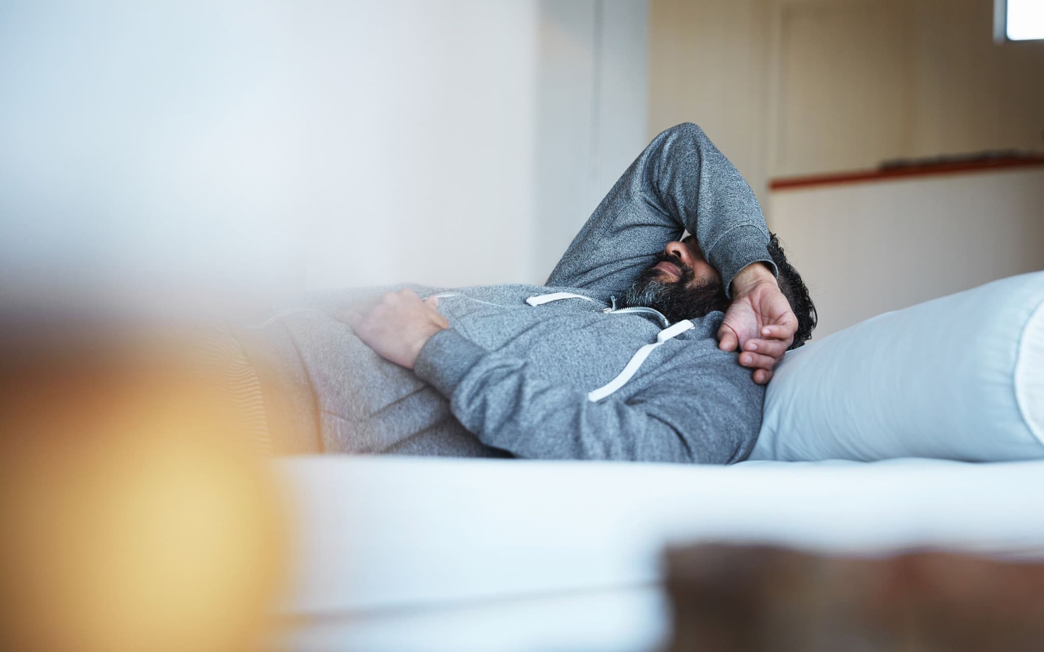 Grippe: Man liegt im Bett und hält sich Hand vor den Kopf.