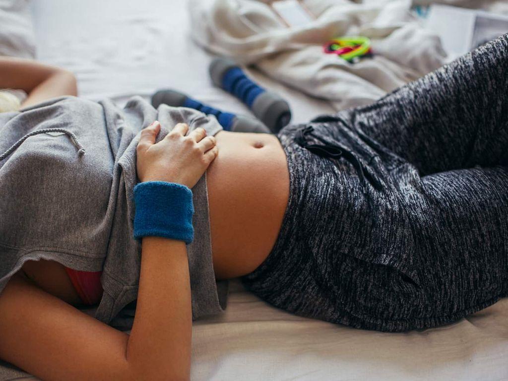 Sport bei Regelschmerzen: Frau in Sportkleidung, die sich auf ihrem Bett ausruht