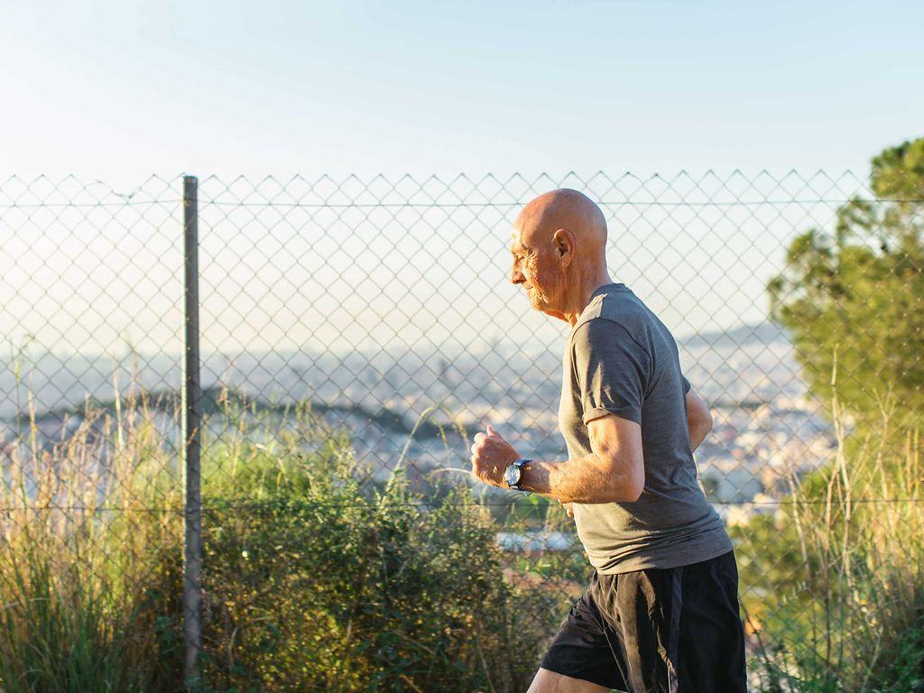 Koronare Herzkrankheit: Älterer Mann joggt, im Hintergrund ist ein Zaun und ein Stadtpanorama.