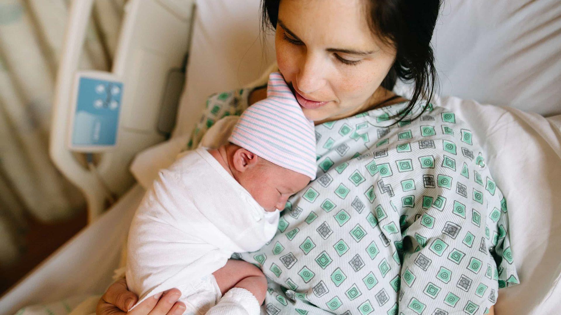 Ort der Geburt: Junge Frau liegt auf einem Krankenhausbett und hält ein Neugeborenes im Arm.