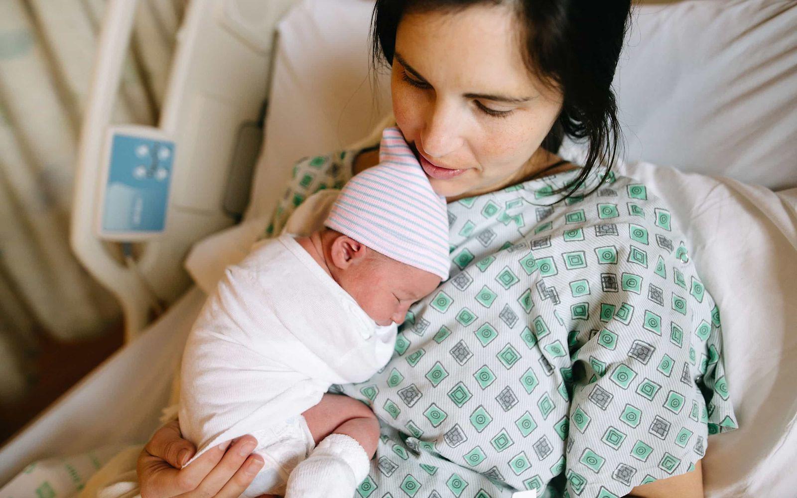 Ort der Geburt: Junge Frau liegt auf einem Krankenhausbett und hält ein Neugeborenes im Arm.