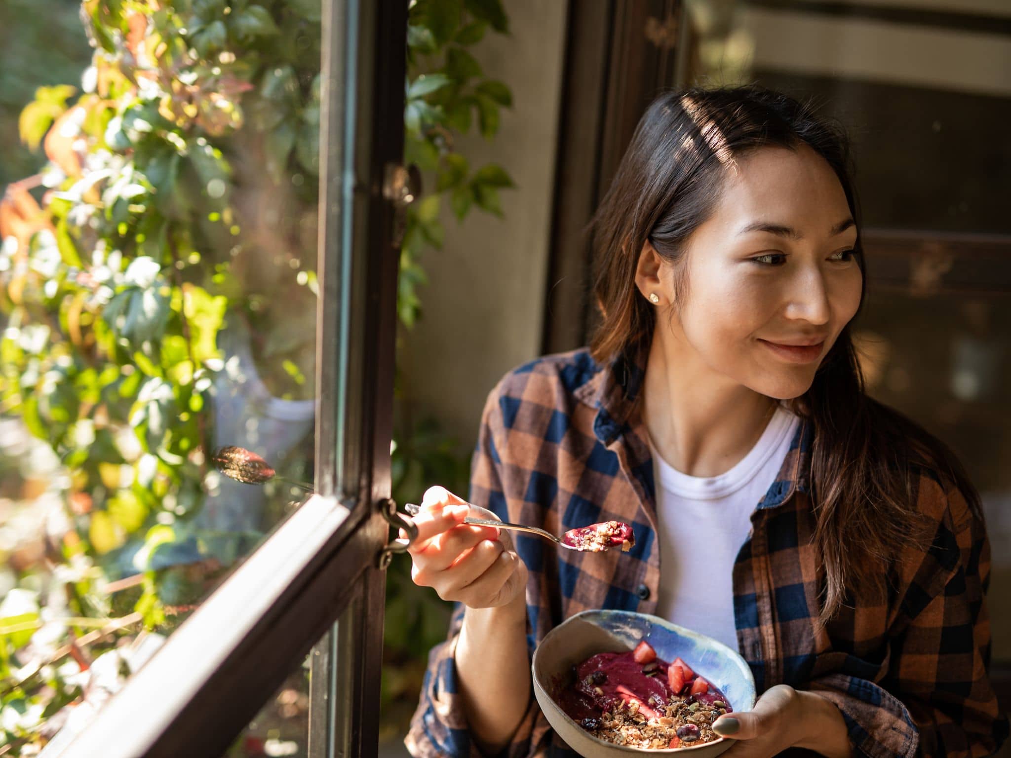 Ernährung bei Schuppenflechte: Junge Frau sitzt am Fenster und isst Müsli