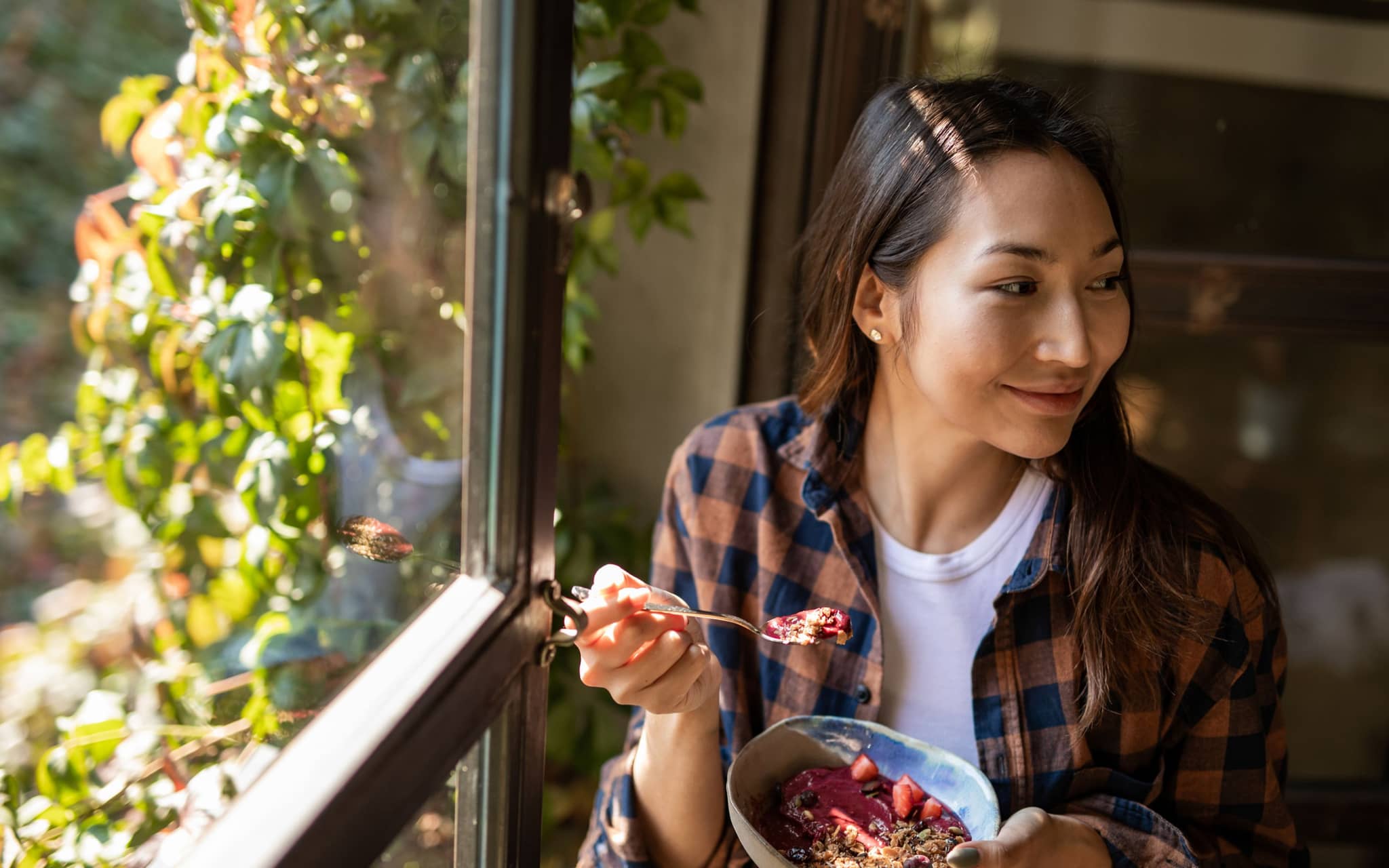 Ernährung bei Schuppenflechte: Junge Frau sitzt am Fenster und isst Müsli