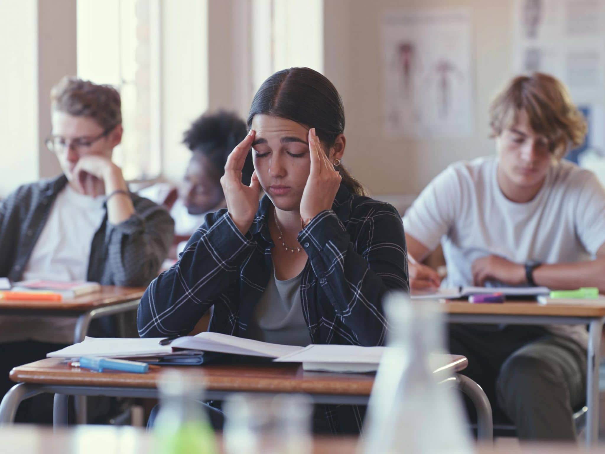 Präventionsradar 2025: Teenagerin sitzt mit geschlossenen Augen in der Schulklasse und hält sich die Hände an die Schläfen.