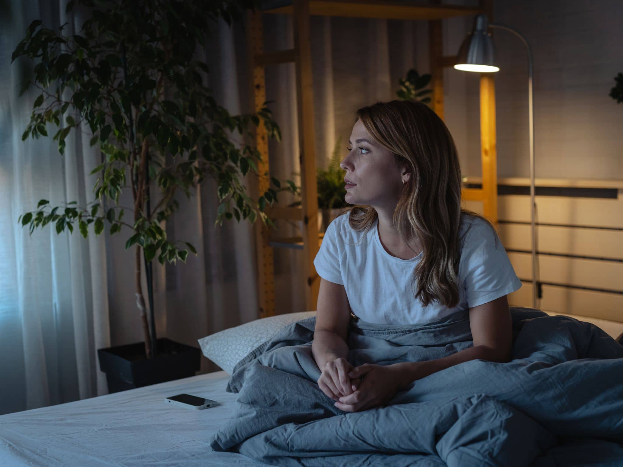 Schlafstörungen in den Wechseljahren: Eine Frau mittleren Alters sitzt auf ihrem Bett und kann nicht schlafen