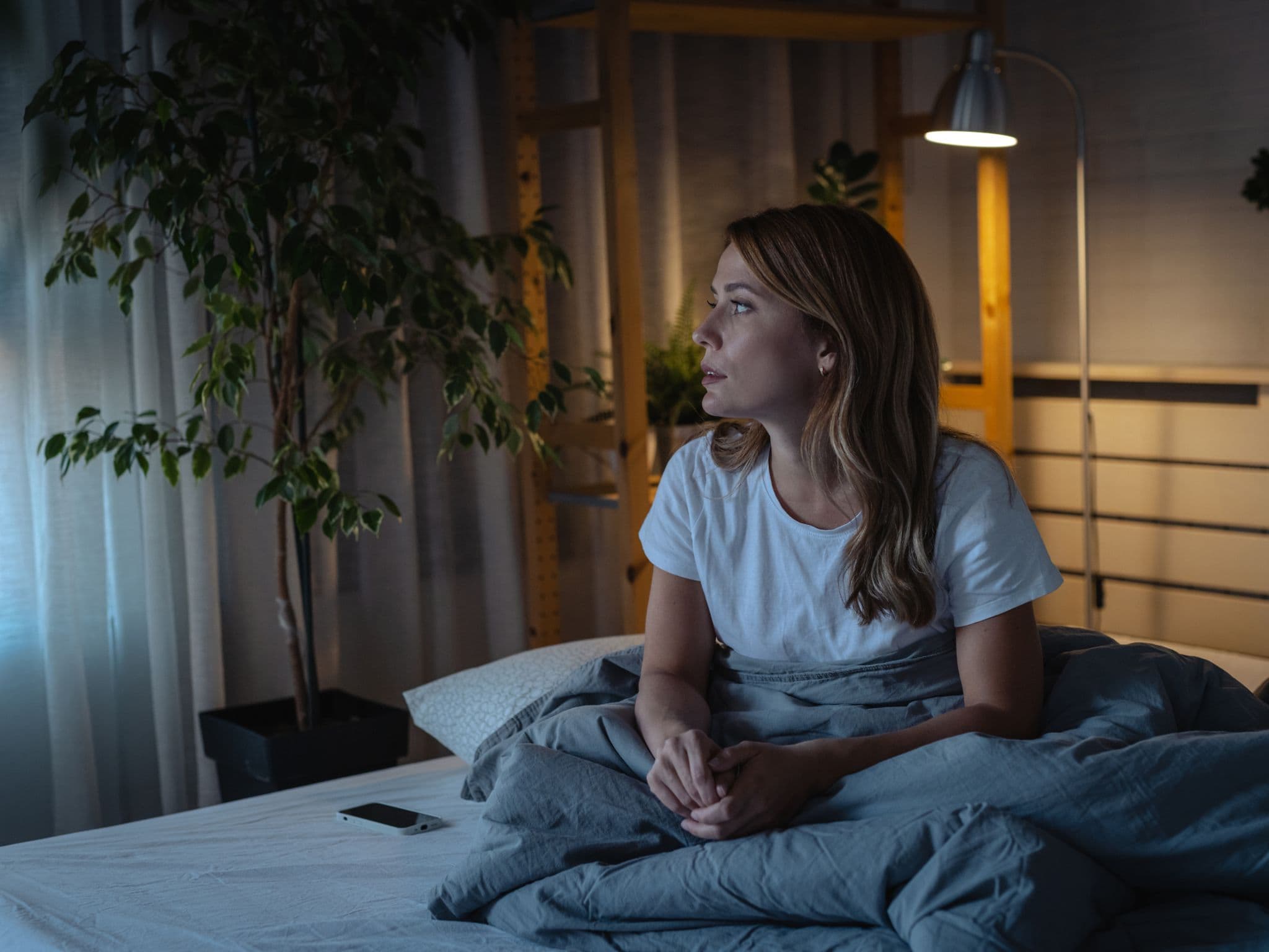 Schlafstörungen in den Wechseljahren: Eine Frau mittleren Alters sitzt auf ihrem Bett und kann nicht schlafen