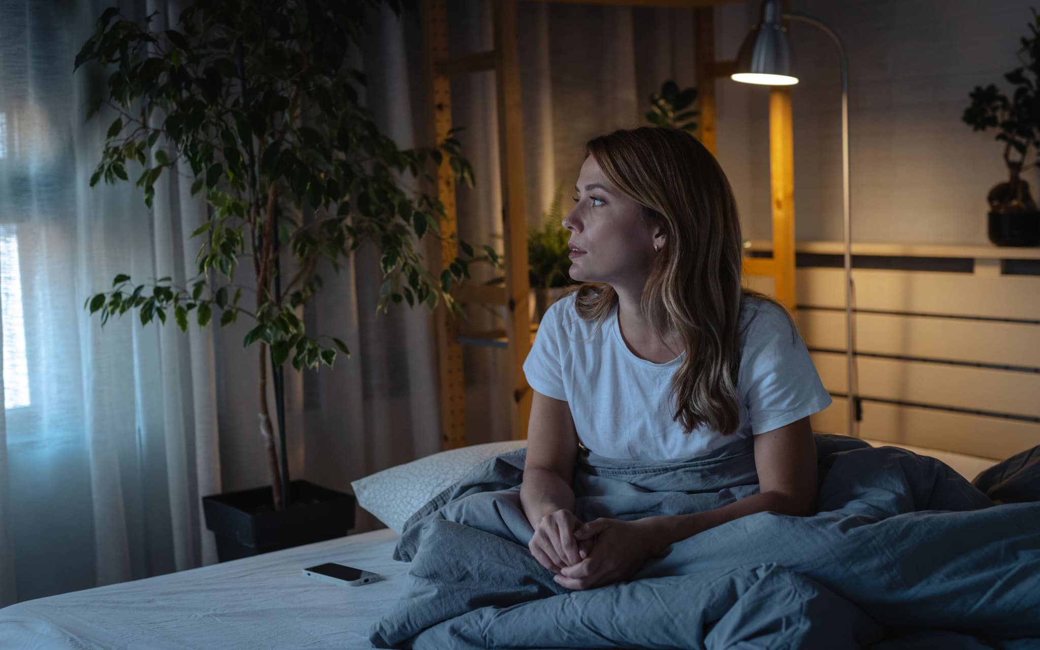 Schlafstörungen in den Wechseljahren: Eine Frau mittleren Alters sitzt auf ihrem Bett und kann nicht schlafen