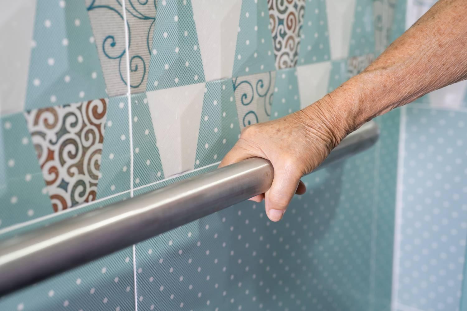 Bade- und Duschhilfen: Hand an einem Handgriff in einem Badezimmer.