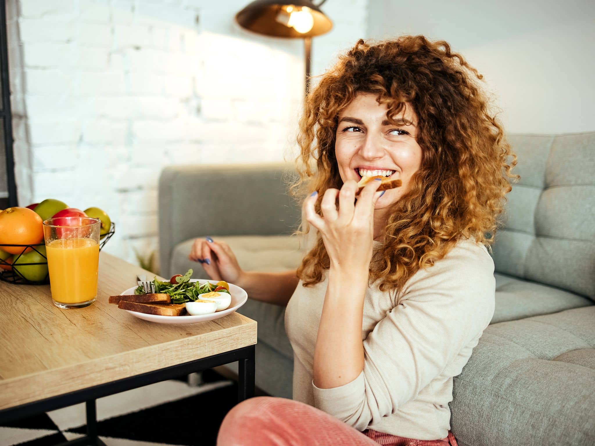 Ernährung bei Hashimoto: Eine Frau sitzt am Couchtisch und isst ein gesundes Frühstück
