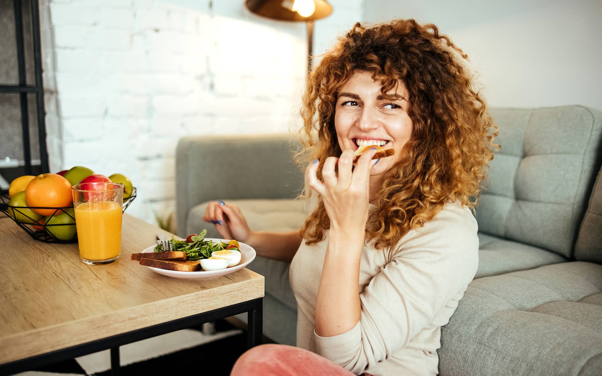 Ernährung bei Hashimoto: Eine Frau sitzt am Couchtisch und isst ein gesundes Frühstück