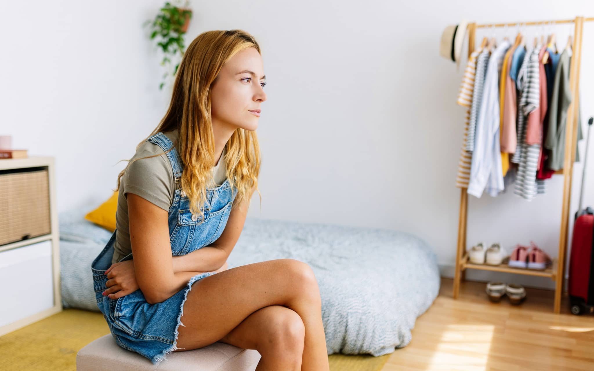 Geschichte der Menstruation: Eine Frau sitzt auf dem Bett und hält sich den Bauch mit den Armen fest