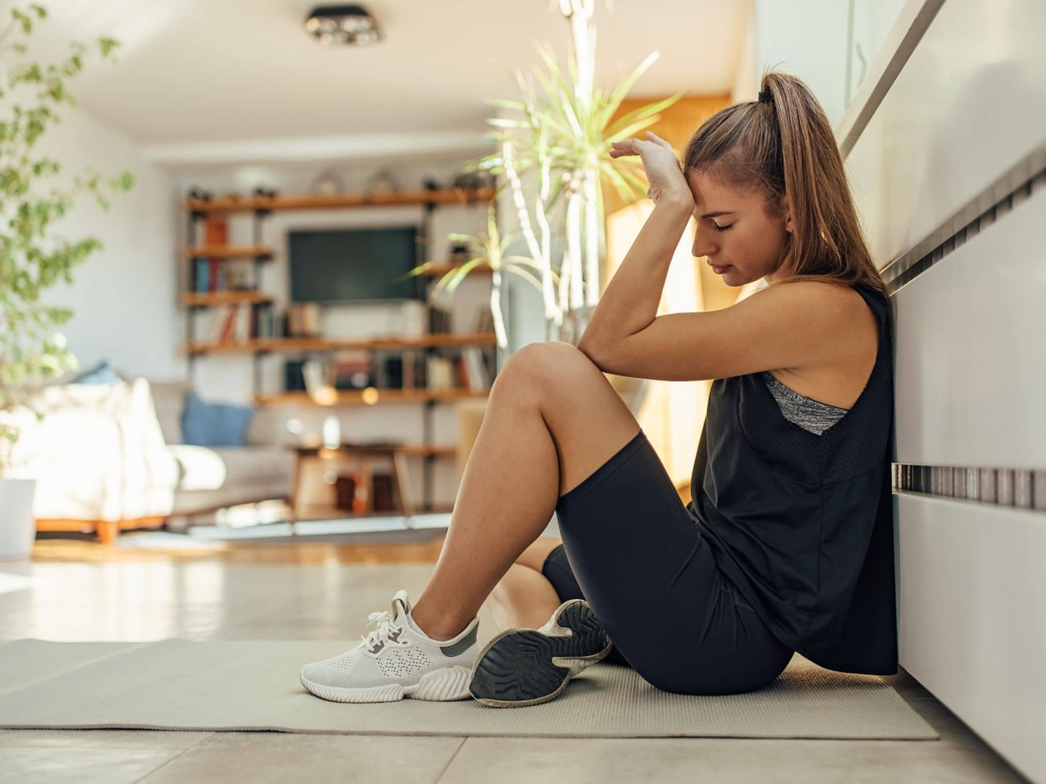 Junge Frau hockt auf dem Küchenboden, weil ihr nach dem Sport übel ist.