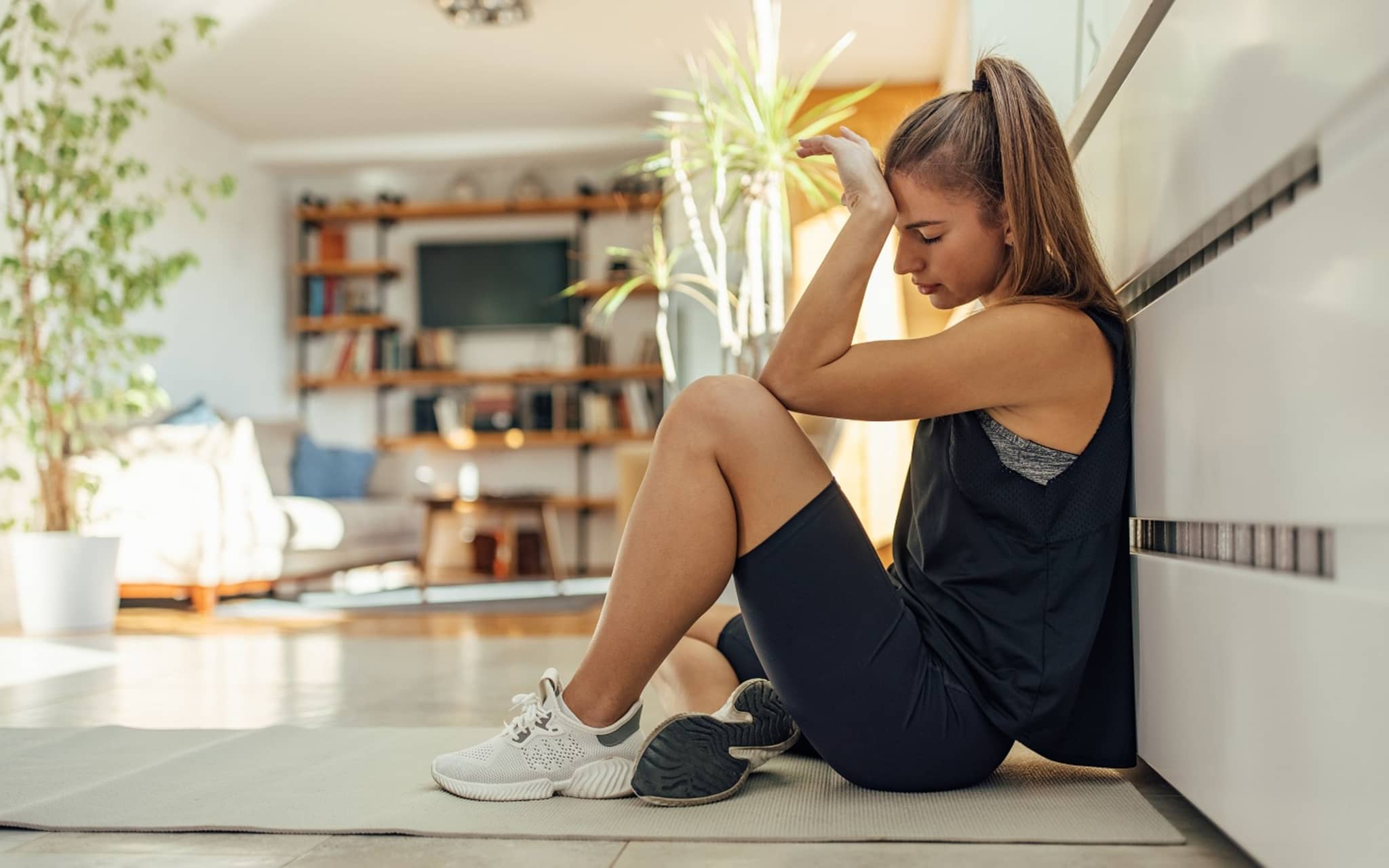 Junge Frau hockt auf dem Küchenboden, weil ihr nach dem Sport übel ist.