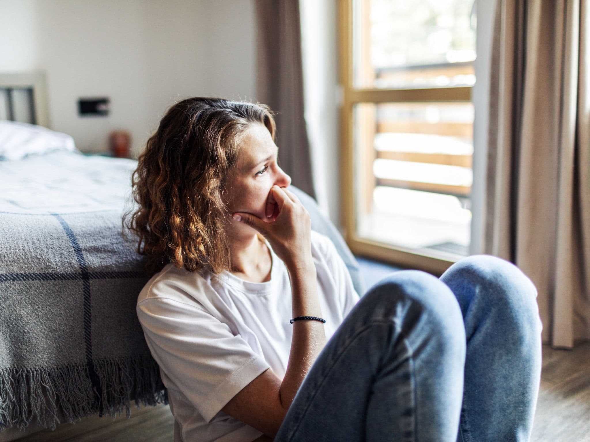 Somatoforme Störung: Eine Frau sitzt auf dem Fußboden ihres Bettes und denkt nach