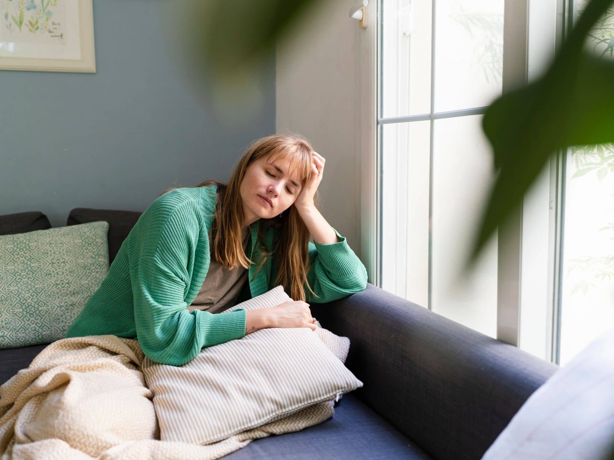 Junge Frau ruht sich auf der Couch aus, weil sie Übelkeit durch Stress empfindet.