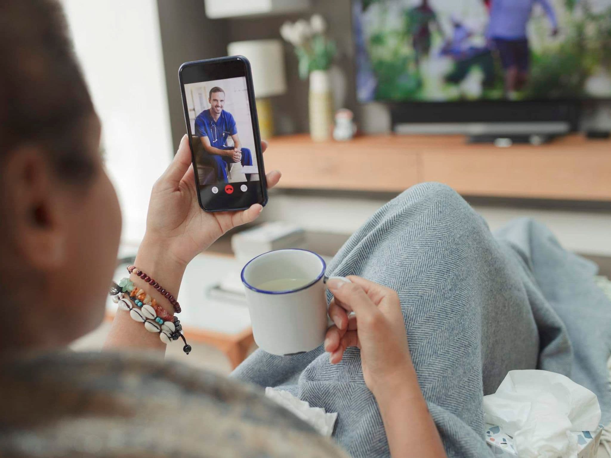 DAK online video consultation: Woman sits on the sofa at home and uses the video consultation.