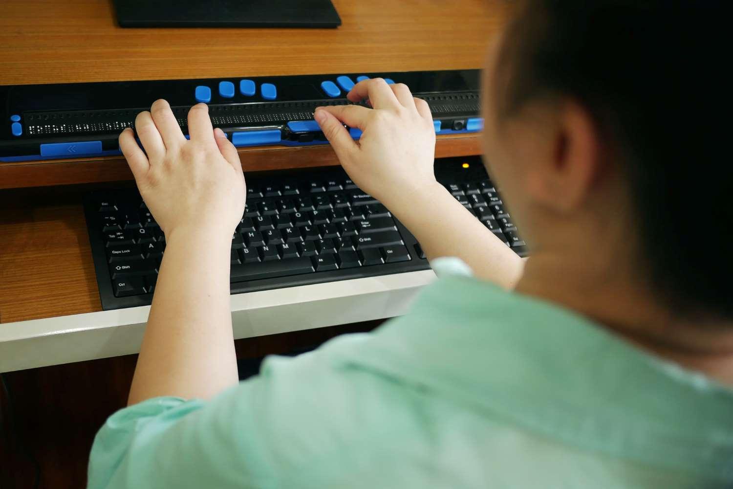 Blindenhilfsmittel: Eine Frau sitzt vor einem Computer und hat die Finger auf einer Braillezeile.