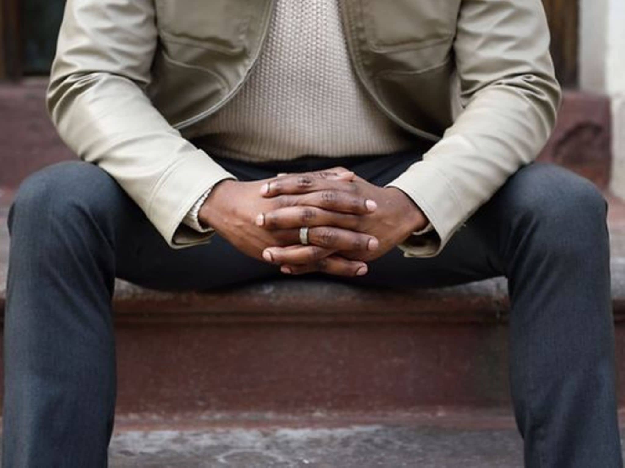 Prostatakrebs: Breitbeinig sitzender Mann mit verschränkten Händen vor dem Schritt.