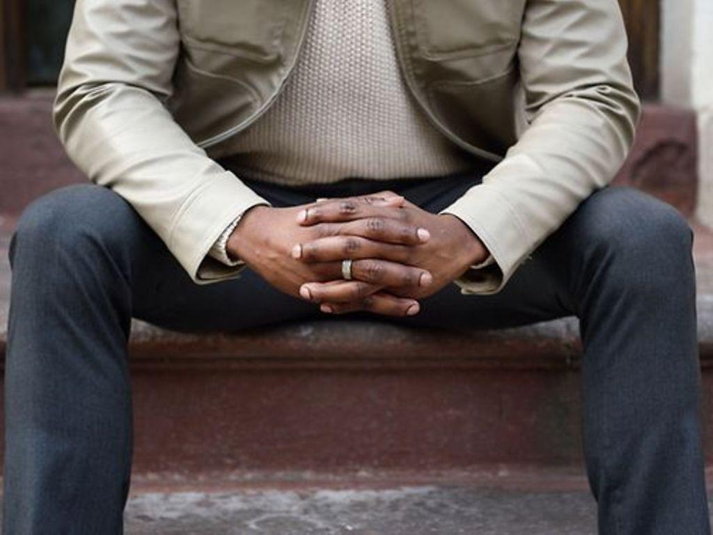 Prostatakrebs: Breitbeinig sitzender Mann mit verschränkten Händen vor dem Schritt.