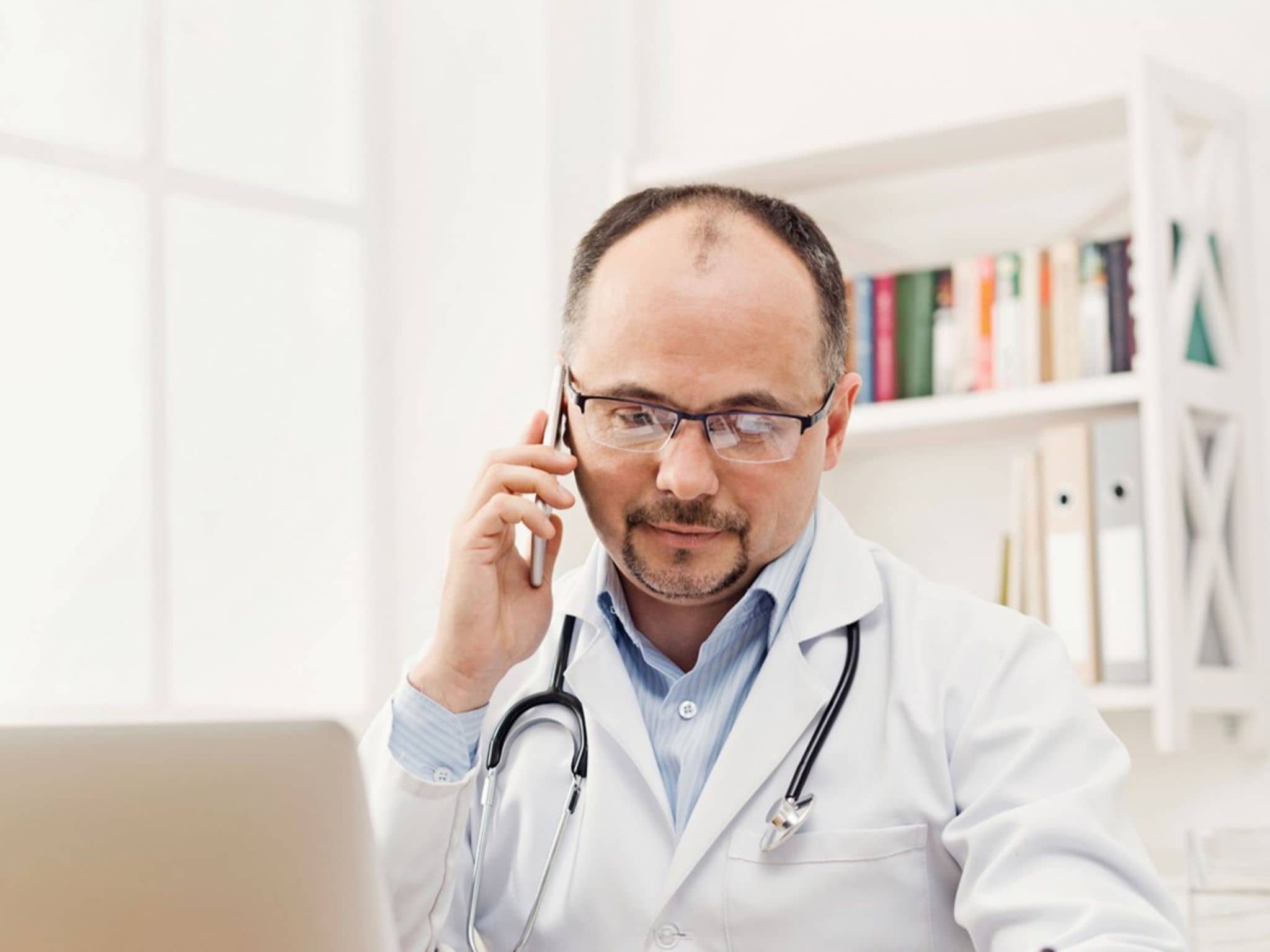 Arzt im Gespräch über Laptop und Handy - die Telemedizin macht's möglich.