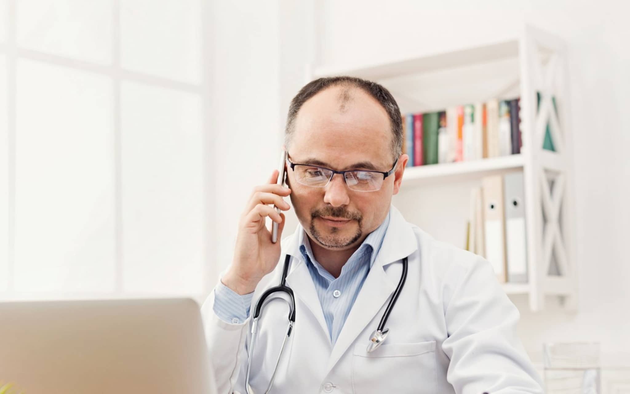 Arzt im Gespräch über Laptop und Handy - die Telemedizin macht's möglich.