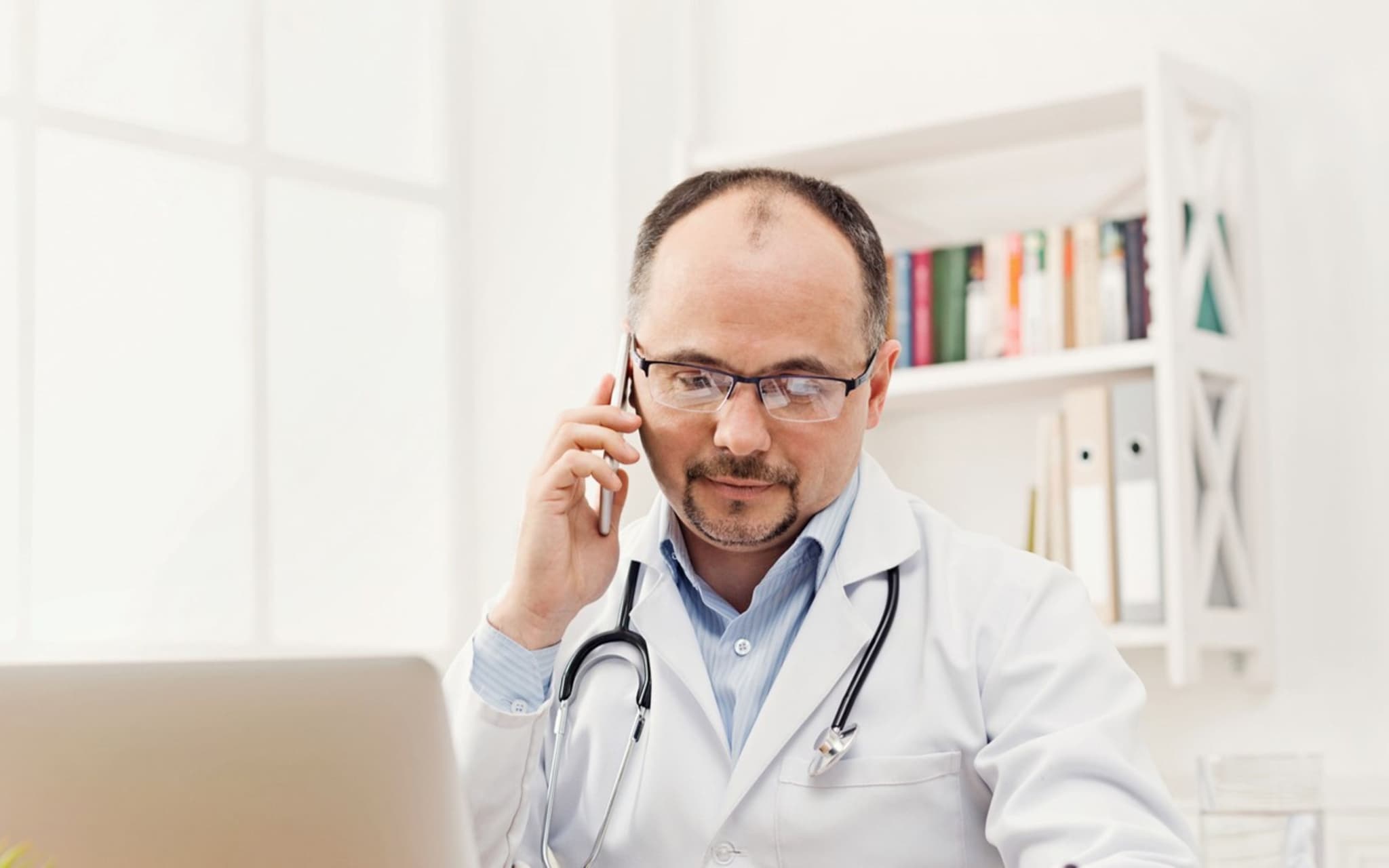 Arzt im Gespräch über Laptop und Handy - die Telemedizin macht's möglich.