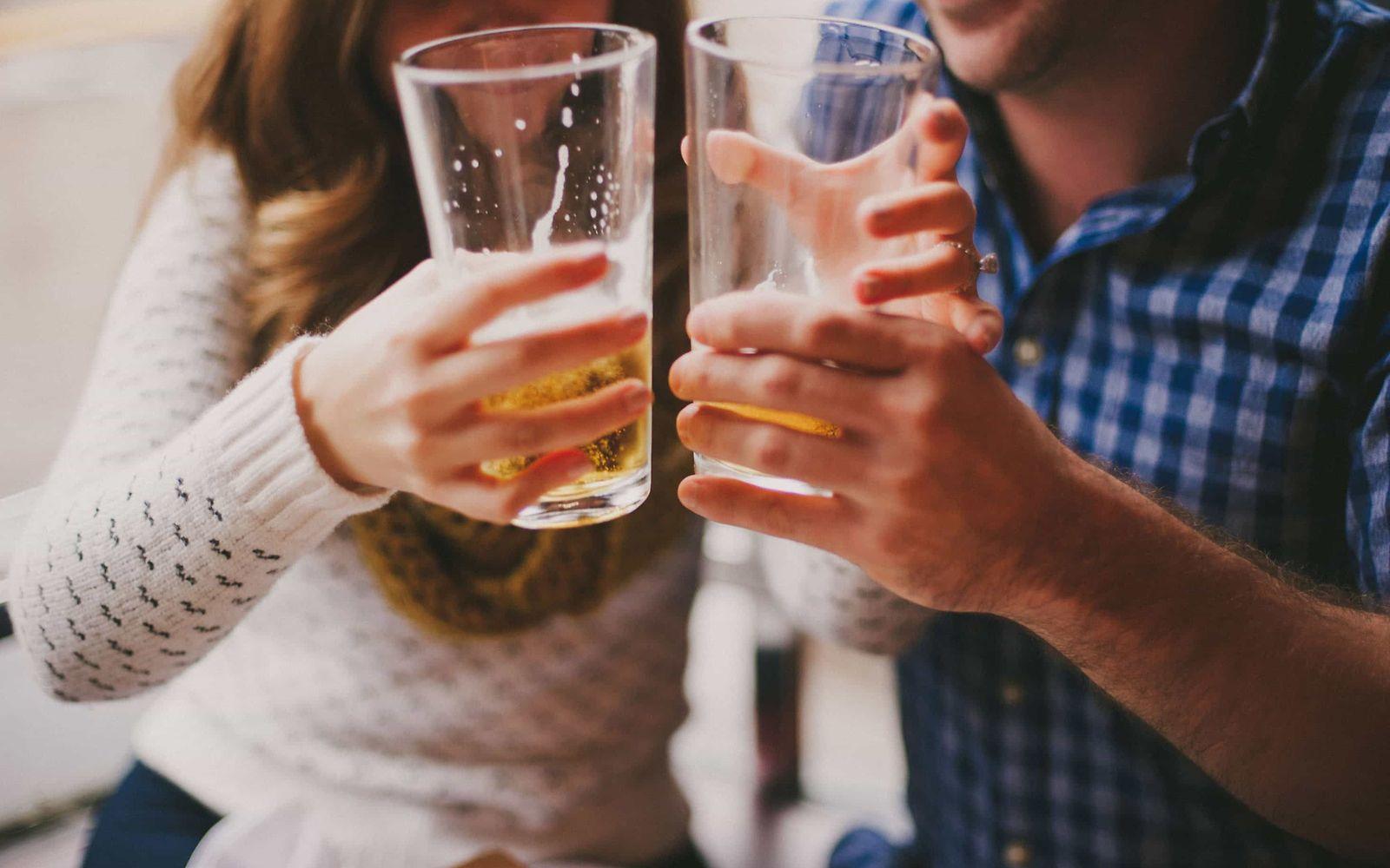 Alkoholsucht: Ein Mann und eine Frau halten zwei halb gefüllte Biergläser aneinander.