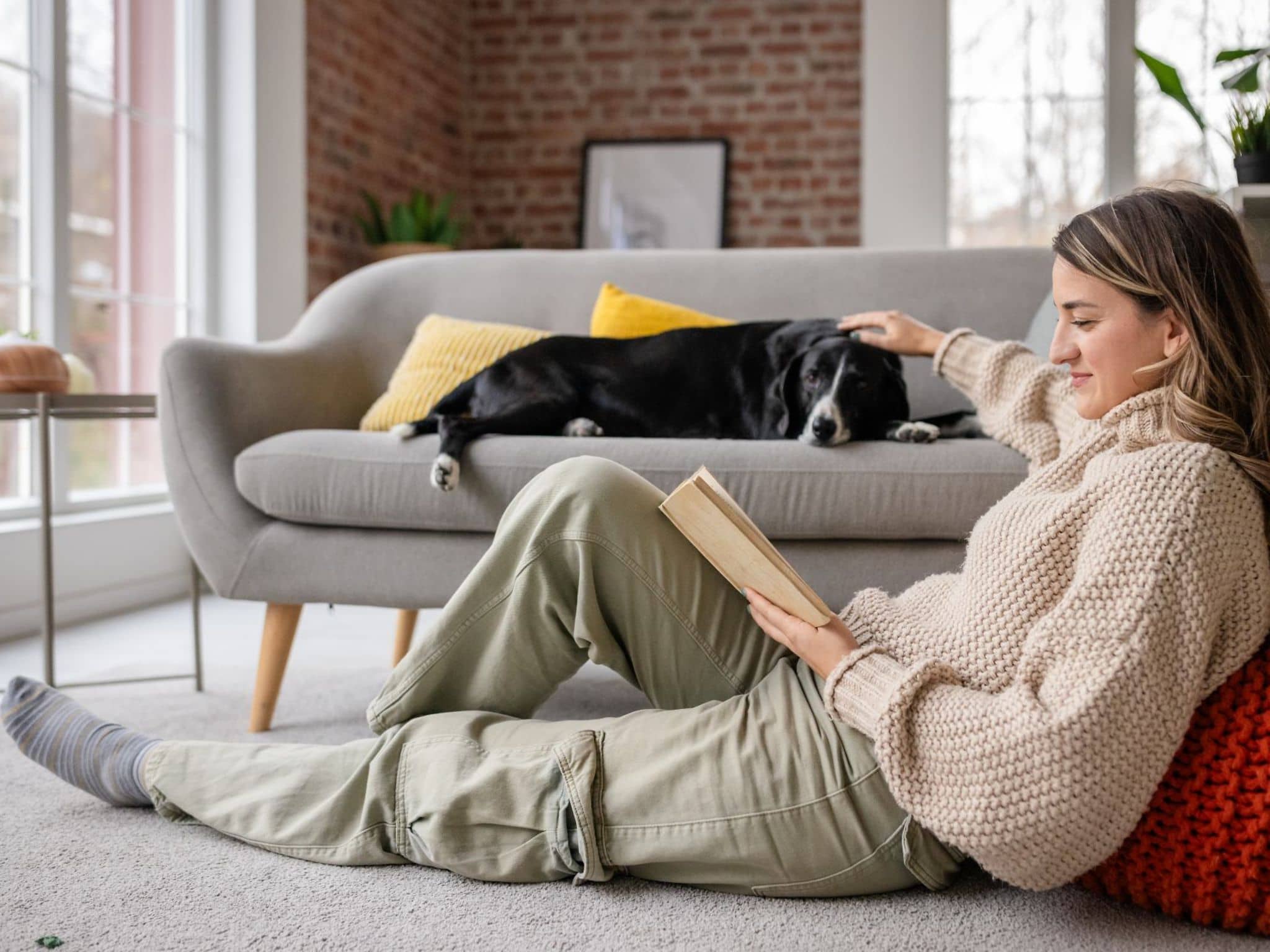 Eine Frau liest ein Buch zur Entspannung und streichelt ihren Hund.