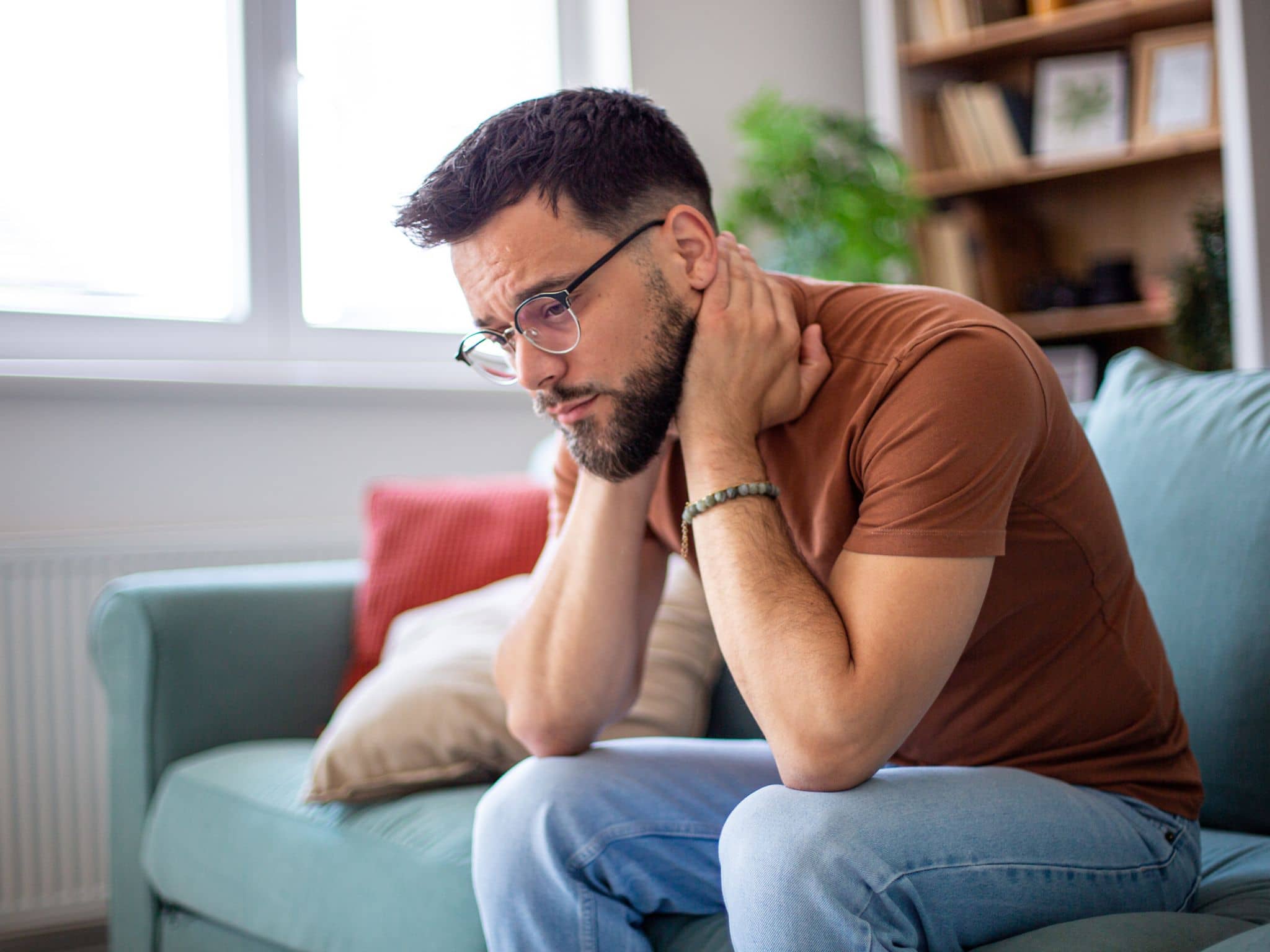 Angststörungen: Ein junger Mann sitzt auf dem Sofa und grübelt