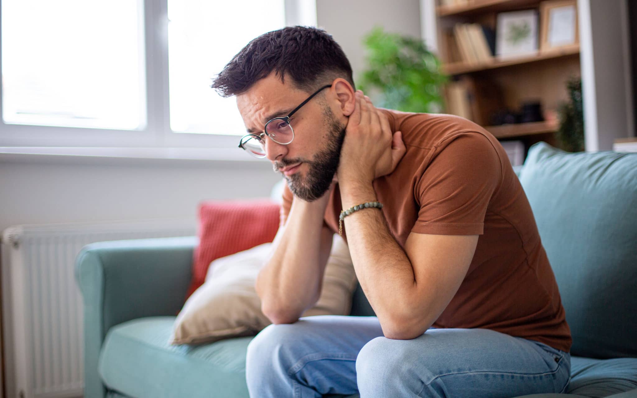 Angststörungen: Ein junger Mann sitzt auf dem Sofa und grübelt
