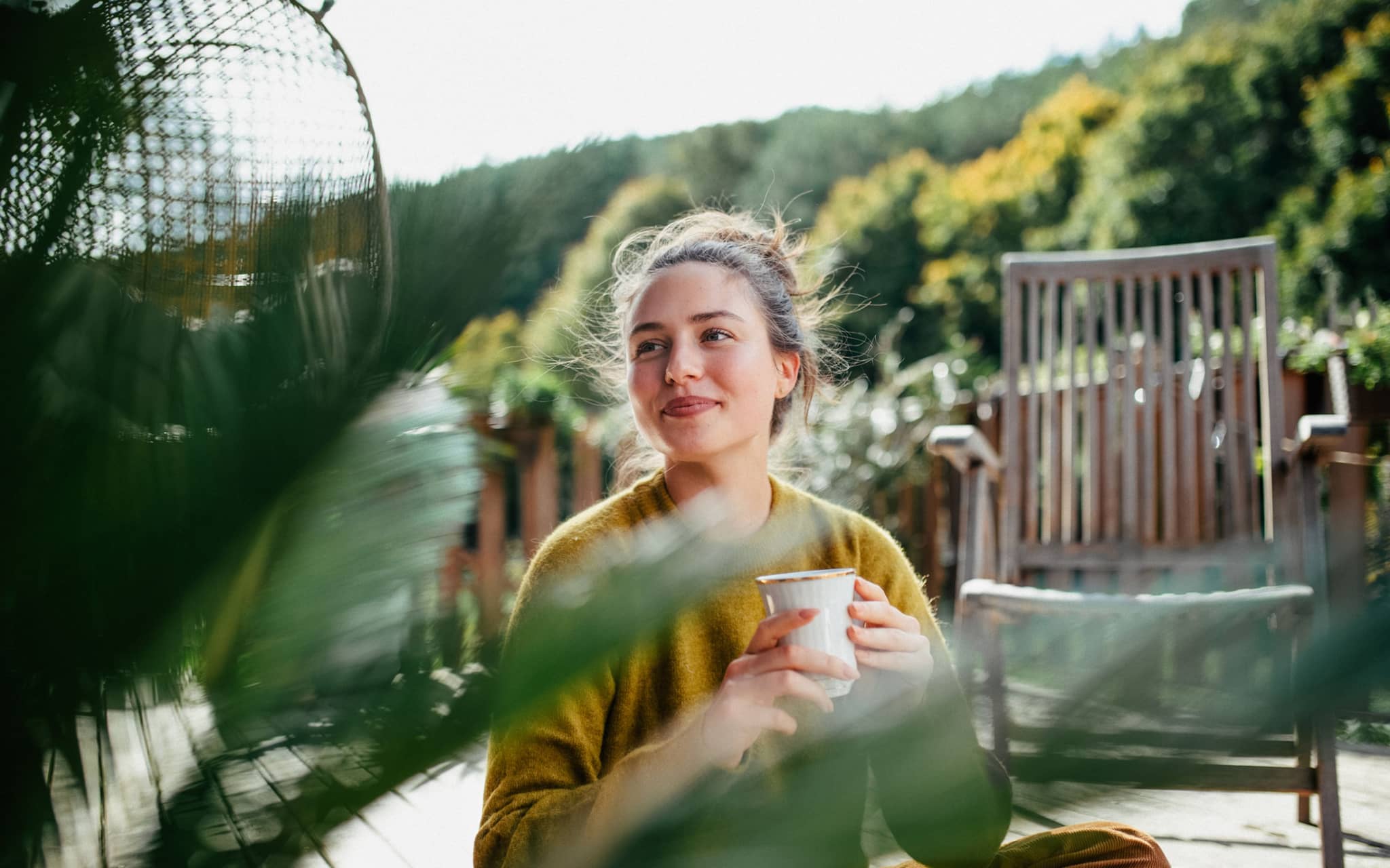 Serotonin erhöhen: Eine Frau sitzt auf einer Terrasse, trinkt Kaffee und lässt sich die Sonne auf die Nase kitzeln