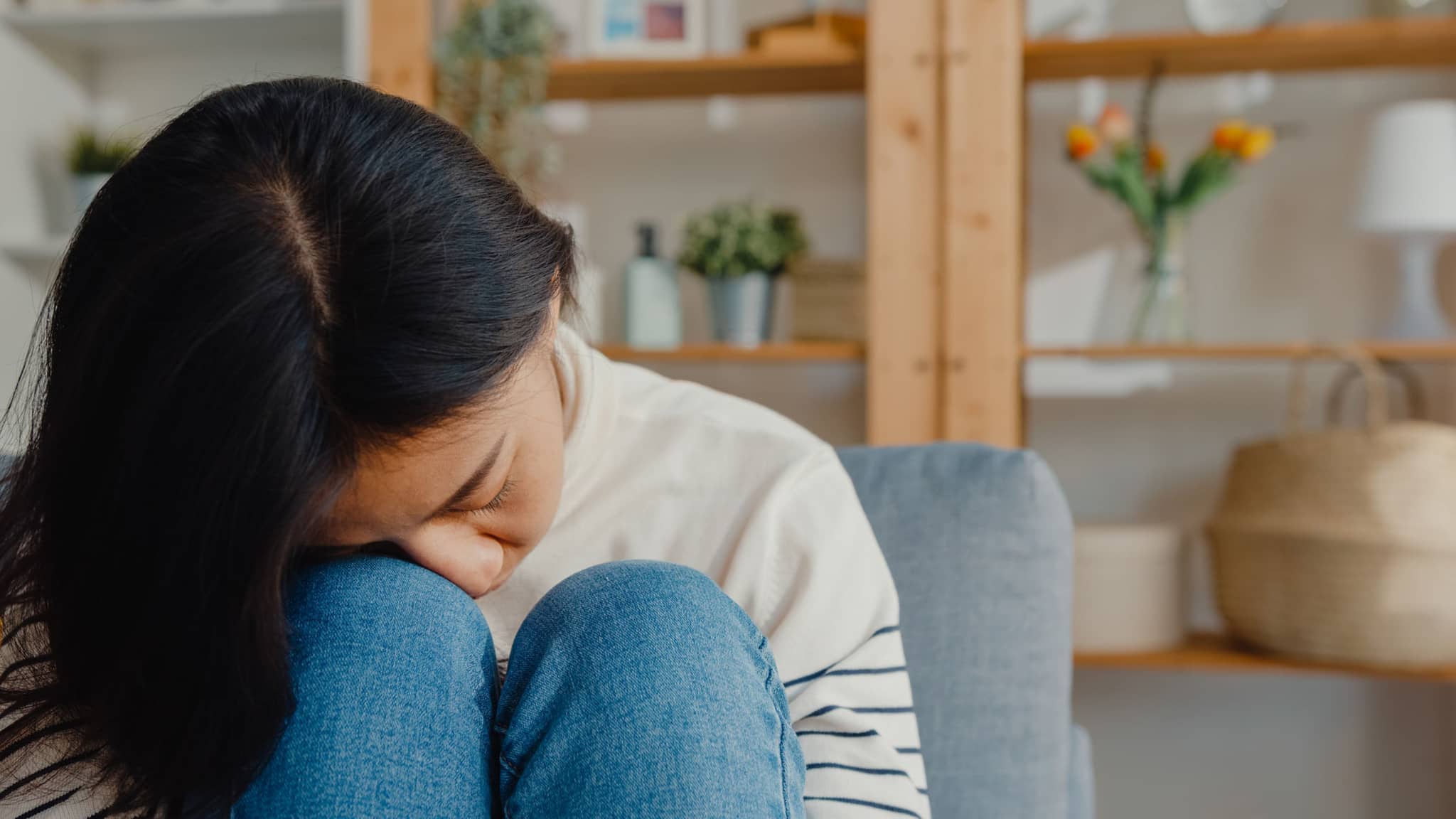 Symptome: Frau legt ihren Kopf auf die Knie in angewinkelter Sitzposition