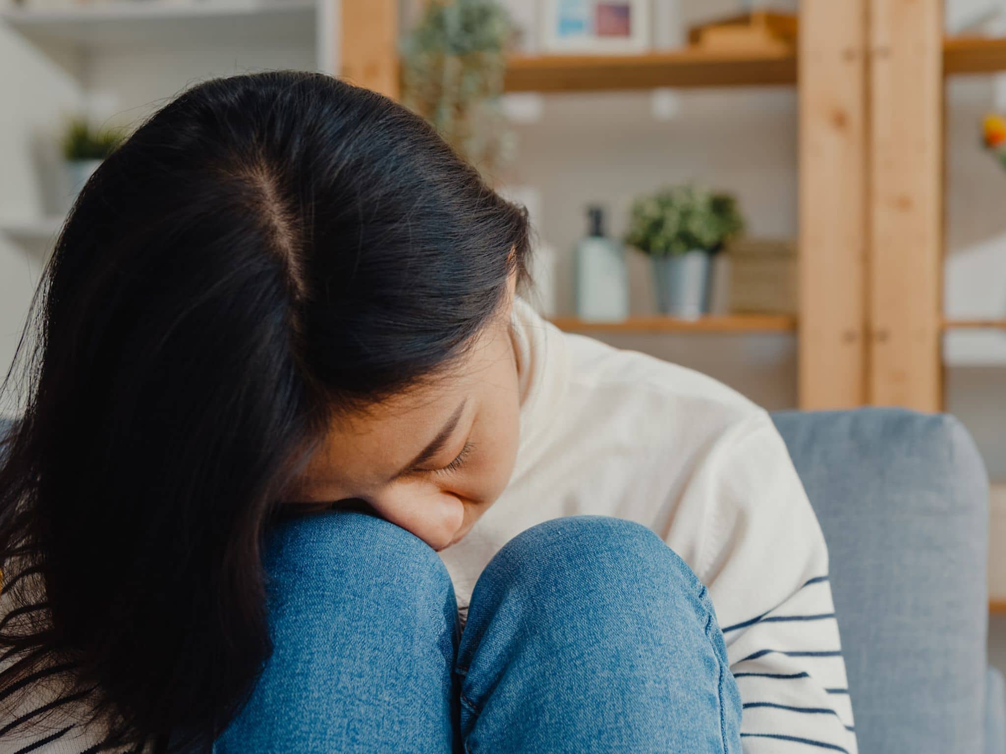 Symptome: Frau legt ihren Kopf auf die Knie in angewinkelter Sitzposition