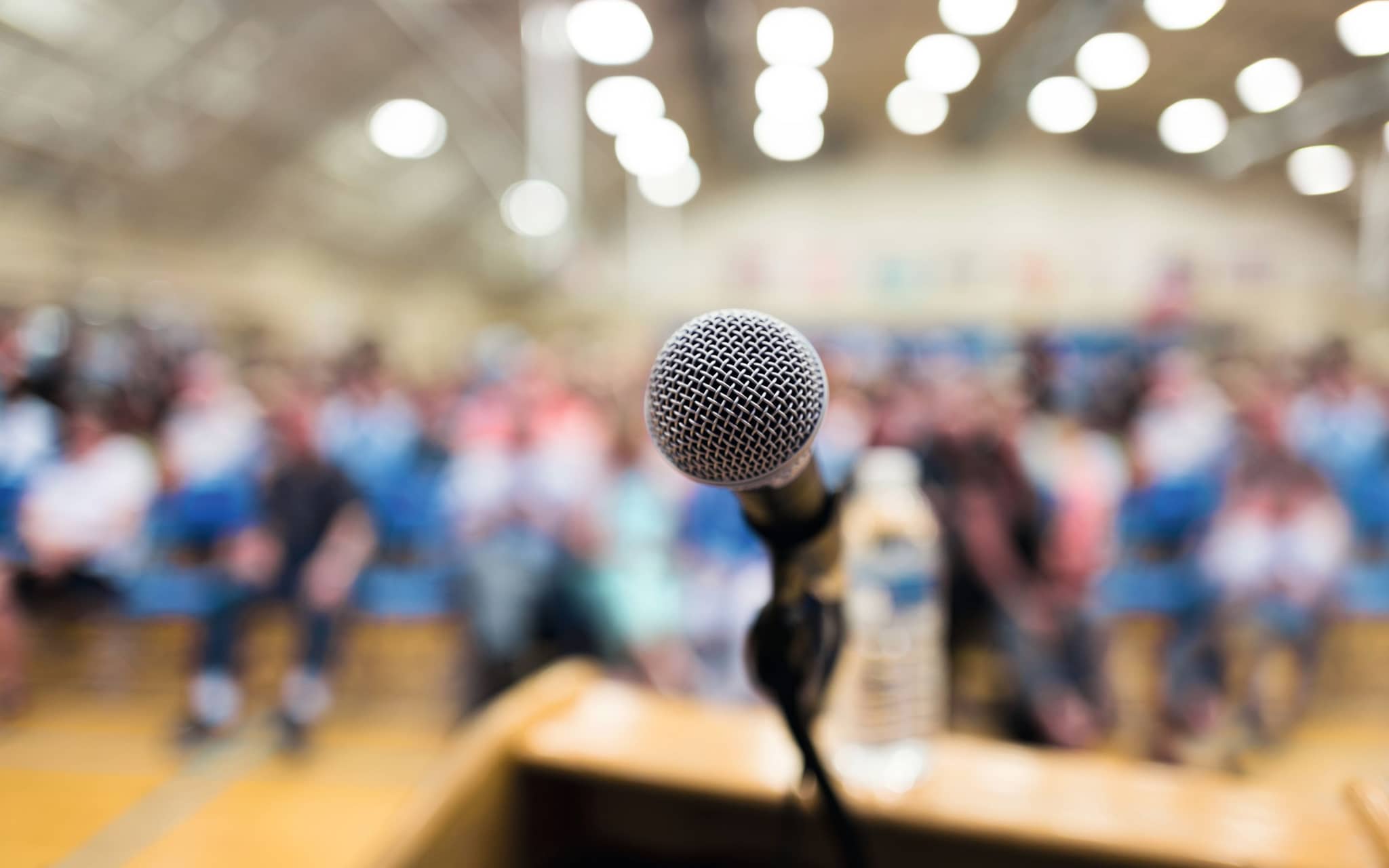 Mikrofon und im Hintergrund verschwommen Puplikum in einem Saal