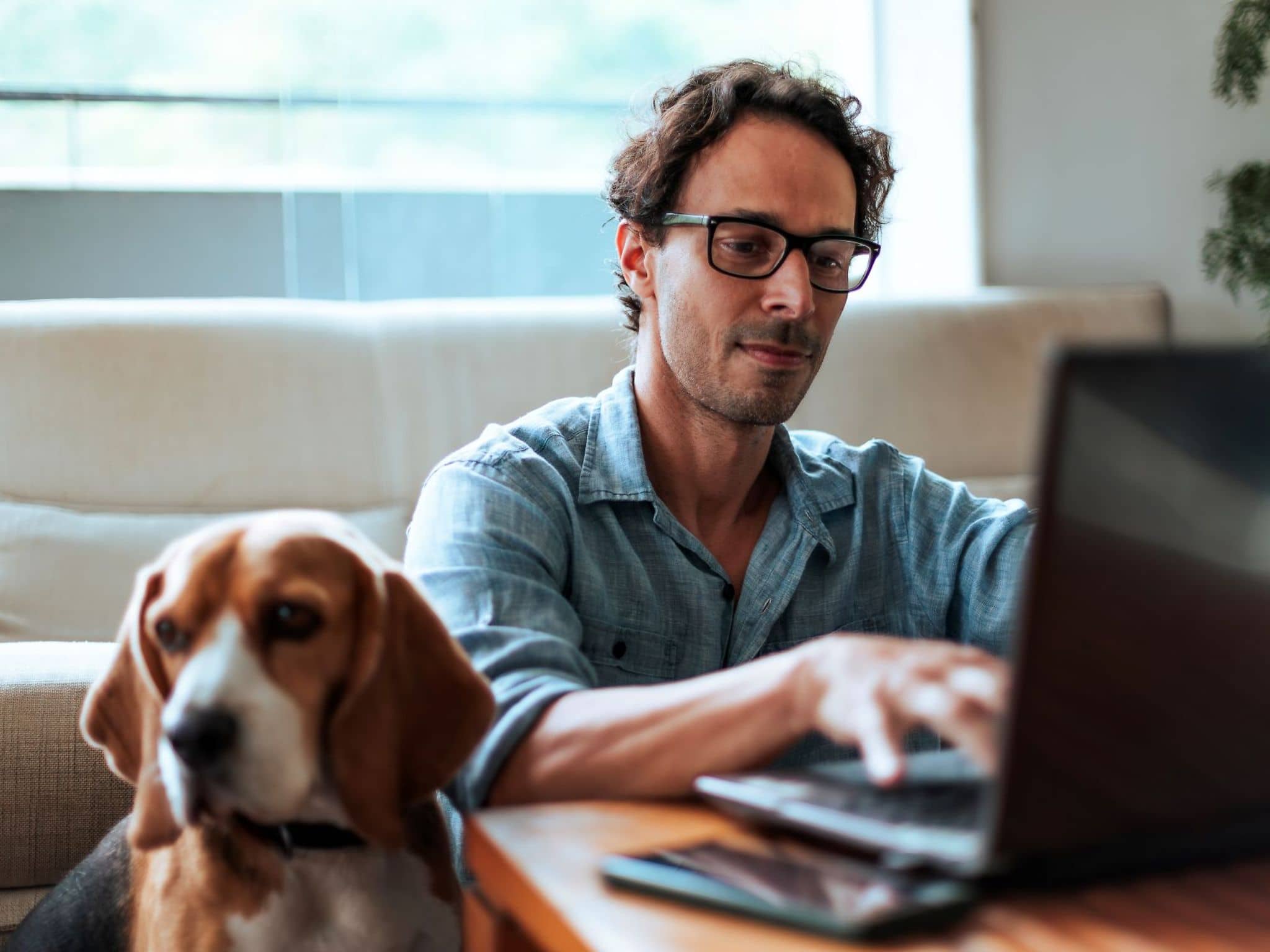 Ein Mann sitzt neben seinem Hund und bestellt Hilfsmittel online am Laptop.