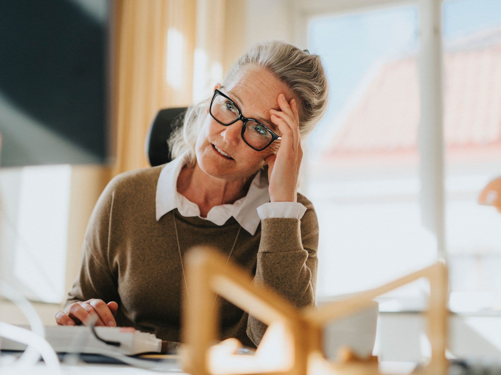 Wechseljahre in Deutschland: Eine ältere Arbeitnehmerin sitzt am Schreibtisch und ist erschöpft
