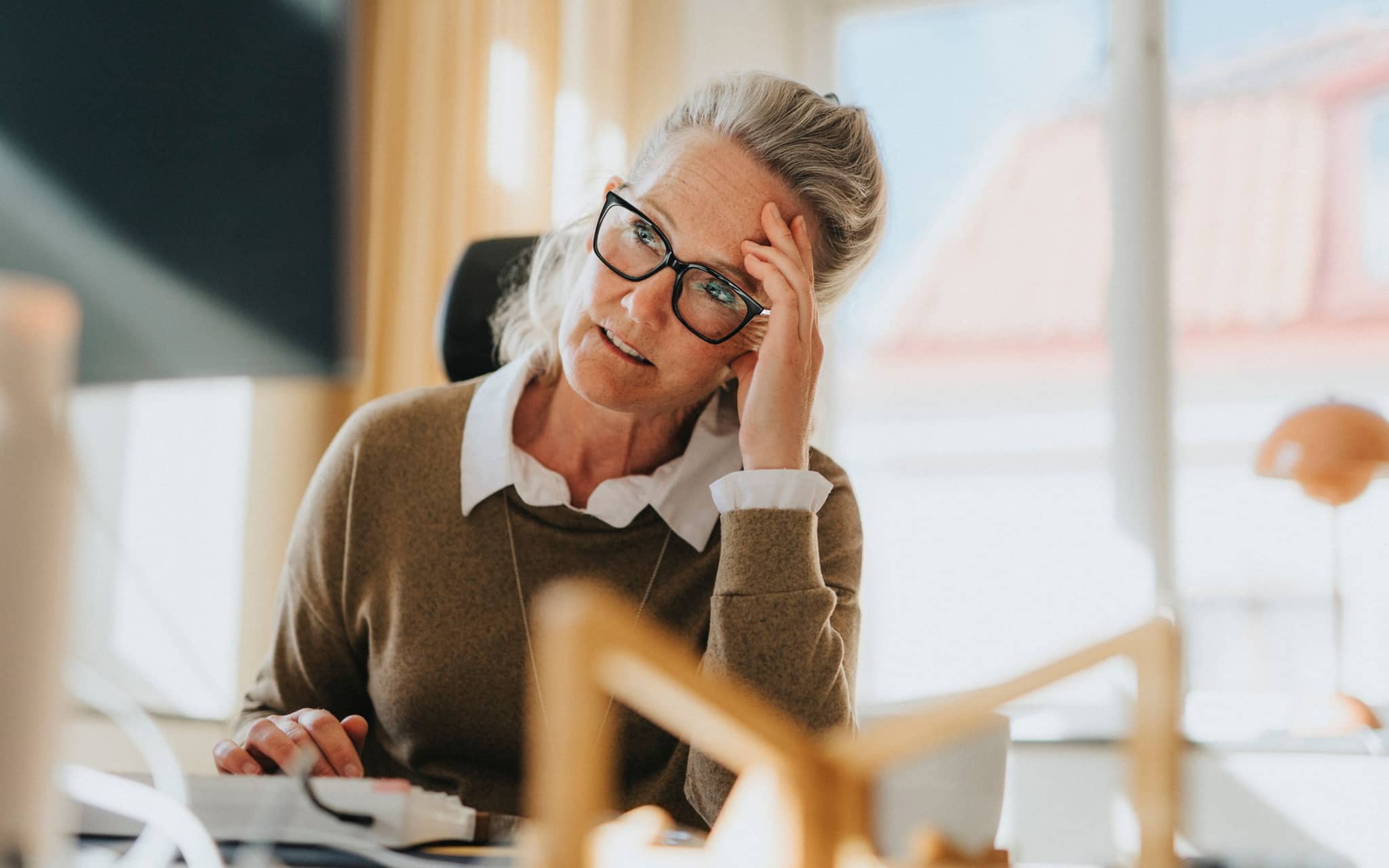 Wechseljahre in Deutschland: Eine ältere Arbeitnehmerin sitzt am Schreibtisch und ist erschöpft