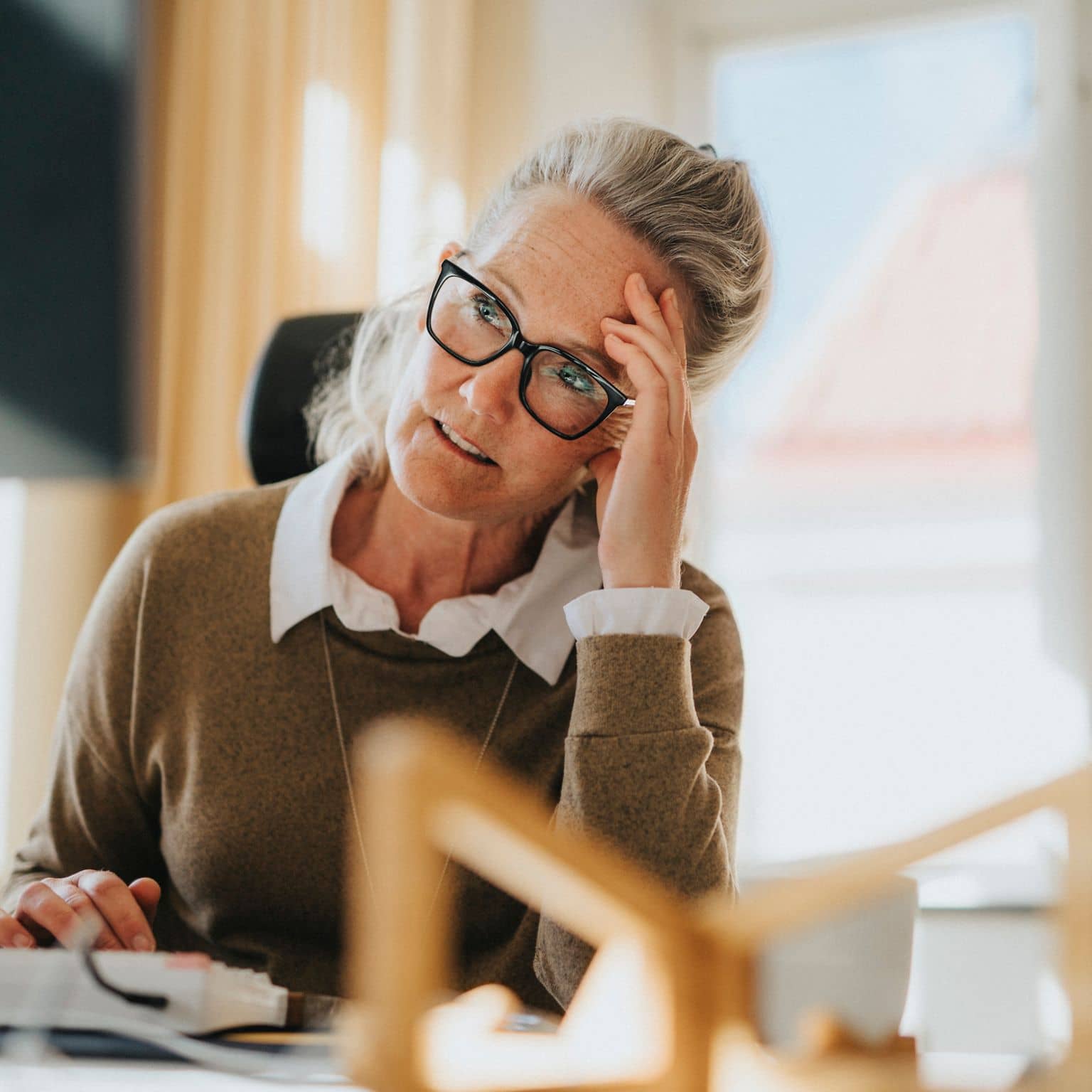 Wechseljahre in Deutschland: Eine ältere Arbeitnehmerin sitzt am Schreibtisch und ist erschöpft