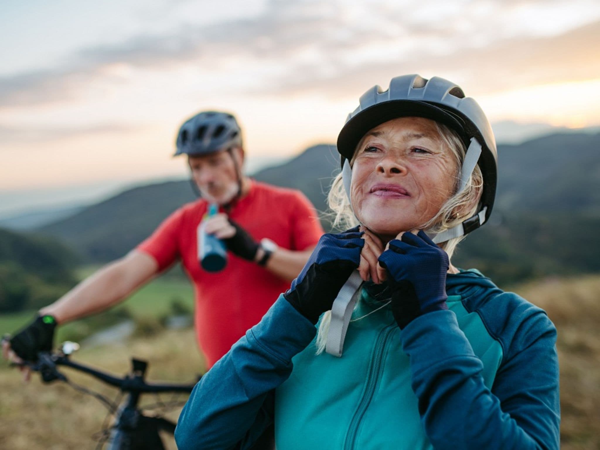 Älteres Paar bei einem Fahrradausflug, sie richtet ihren Helm.