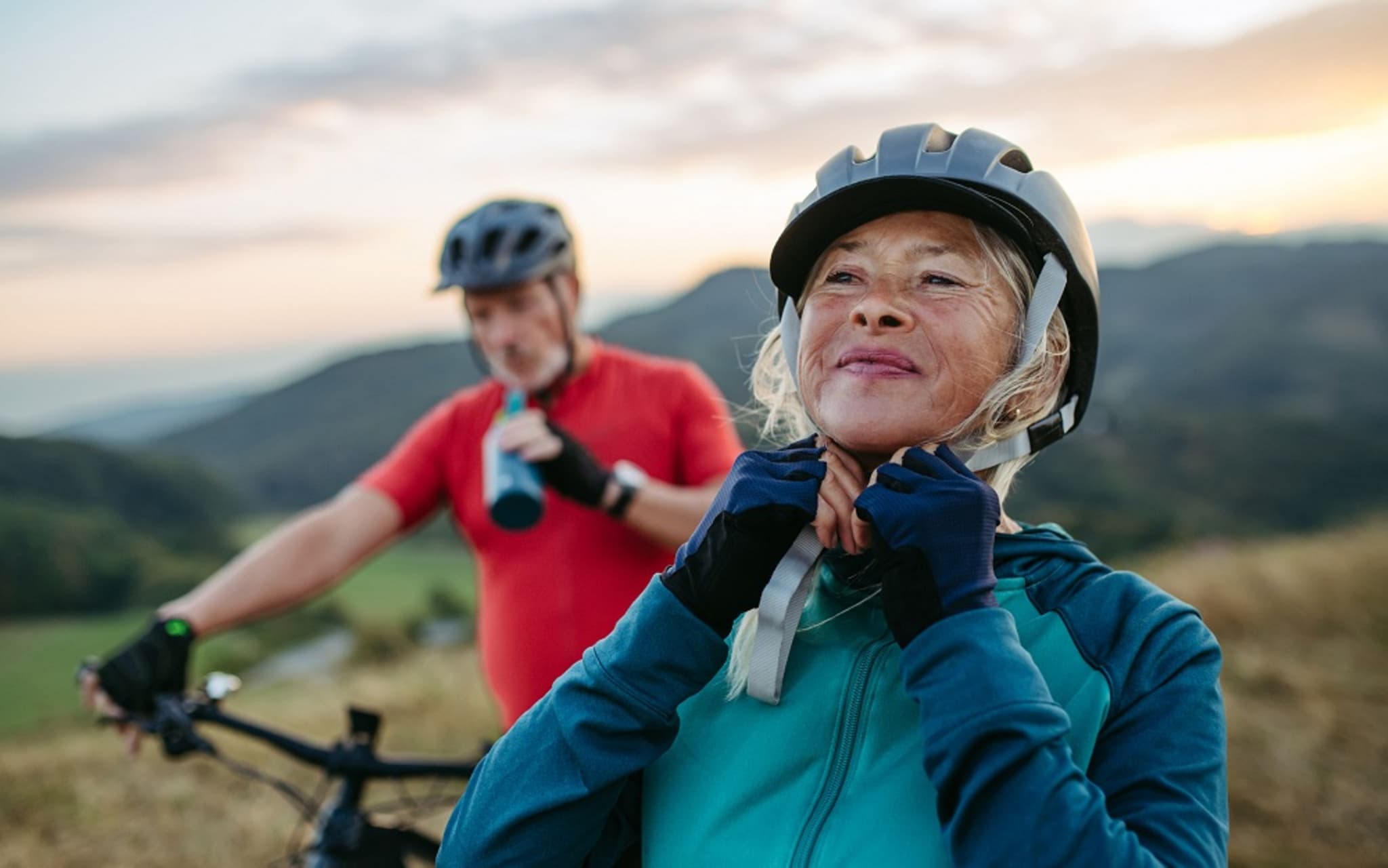 Älteres Paar bei einem Fahrradausflug, sie richtet ihren Helm.