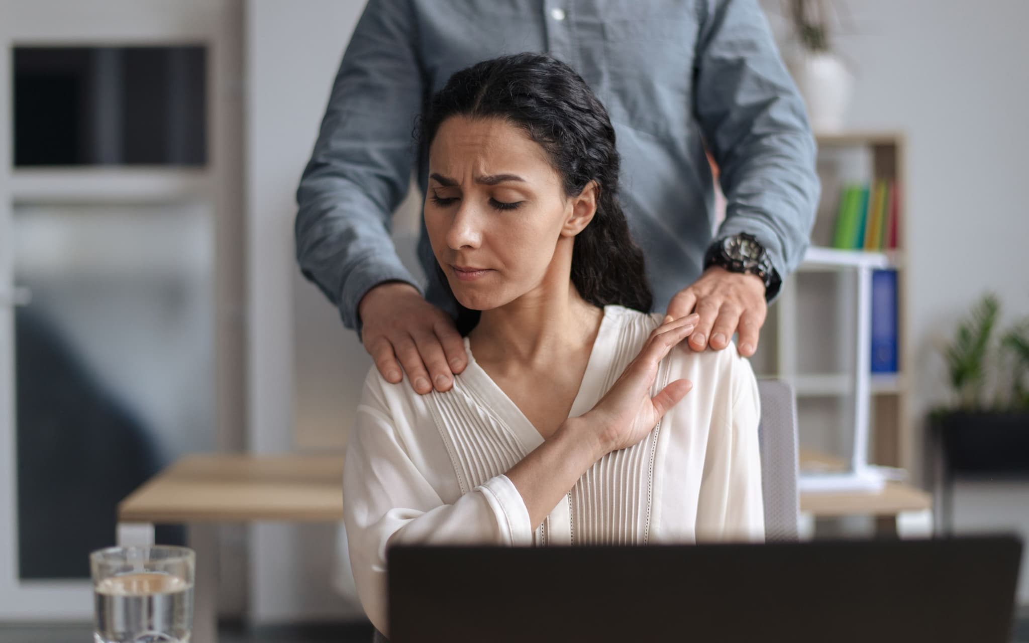 Wann beginnt sexuelle Belästigung: Eine Frau, die am Schreibtisch sitzt, wird von einem Mann an den Schultern berührt.
