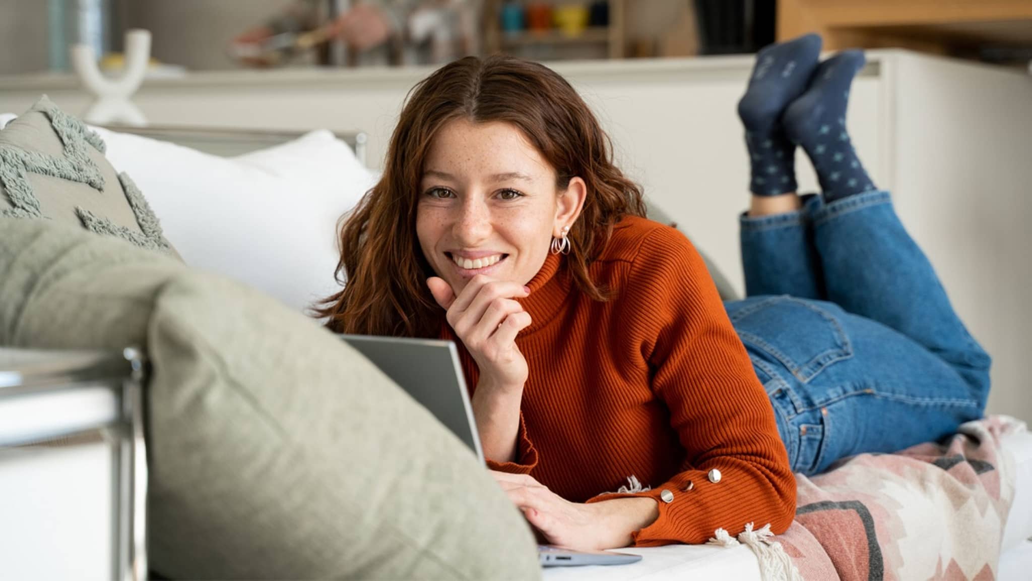DAK-Versicherte liegt bäuchlings auf dem Sofa und lächelt in die Kamera
