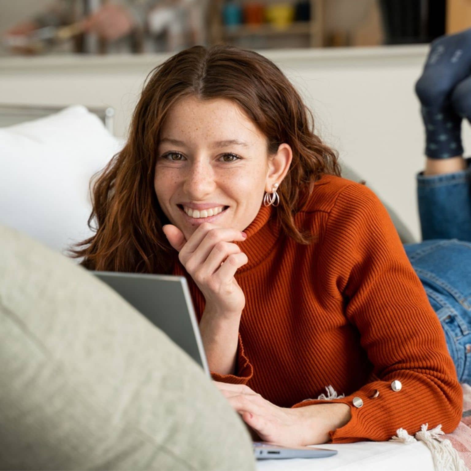 DAK-Versicherte liegt bäuchlings auf dem Sofa und lächelt in die Kamera
