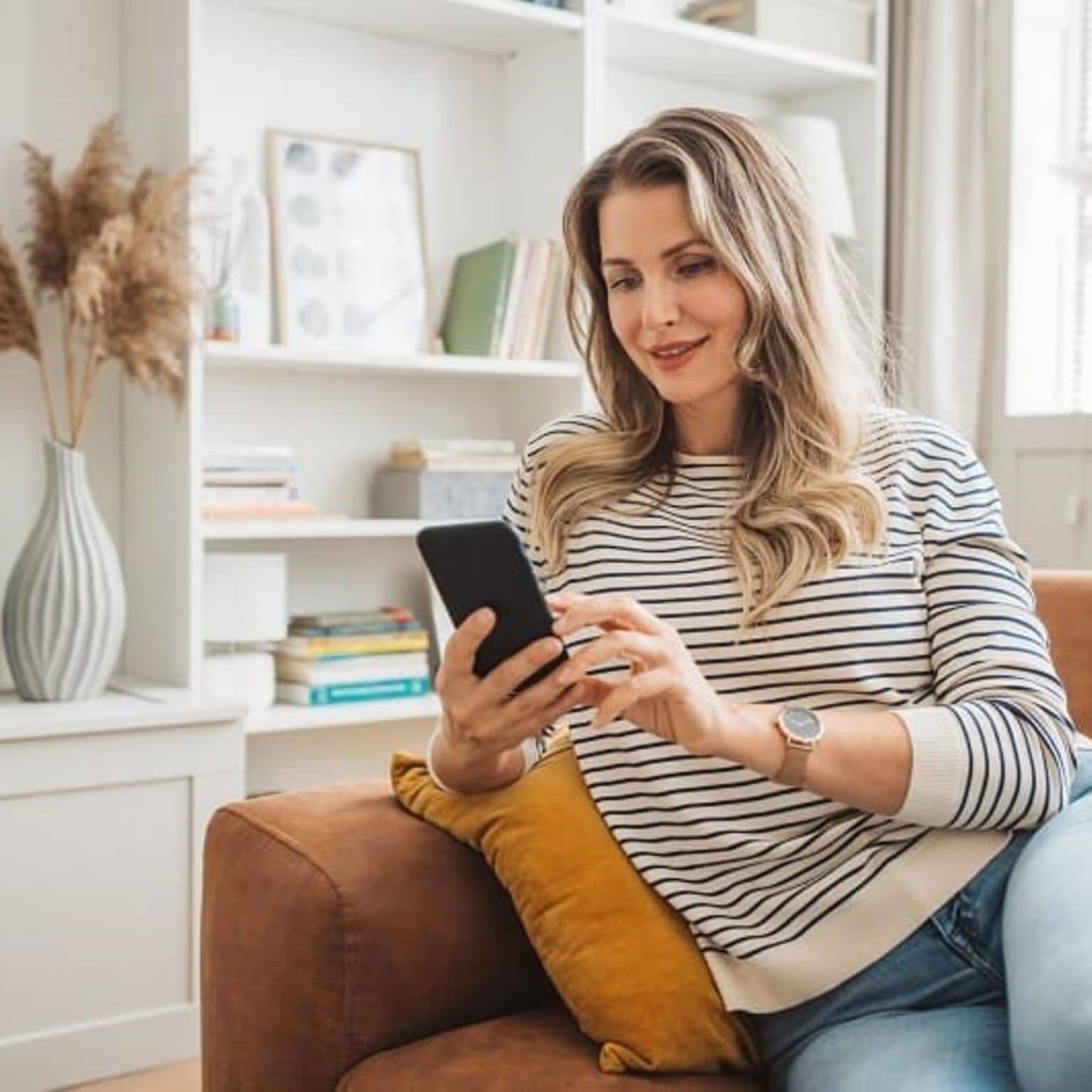 Frau erledigt ihr Anliegen mit dem Handy auf dem Sofa.