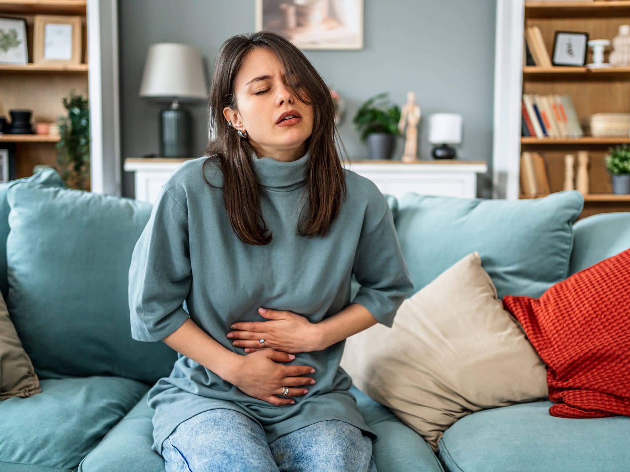Blähungen während der Periode: Eine Frau sitzt auf einem Sofa und hält sich den Bauch fest