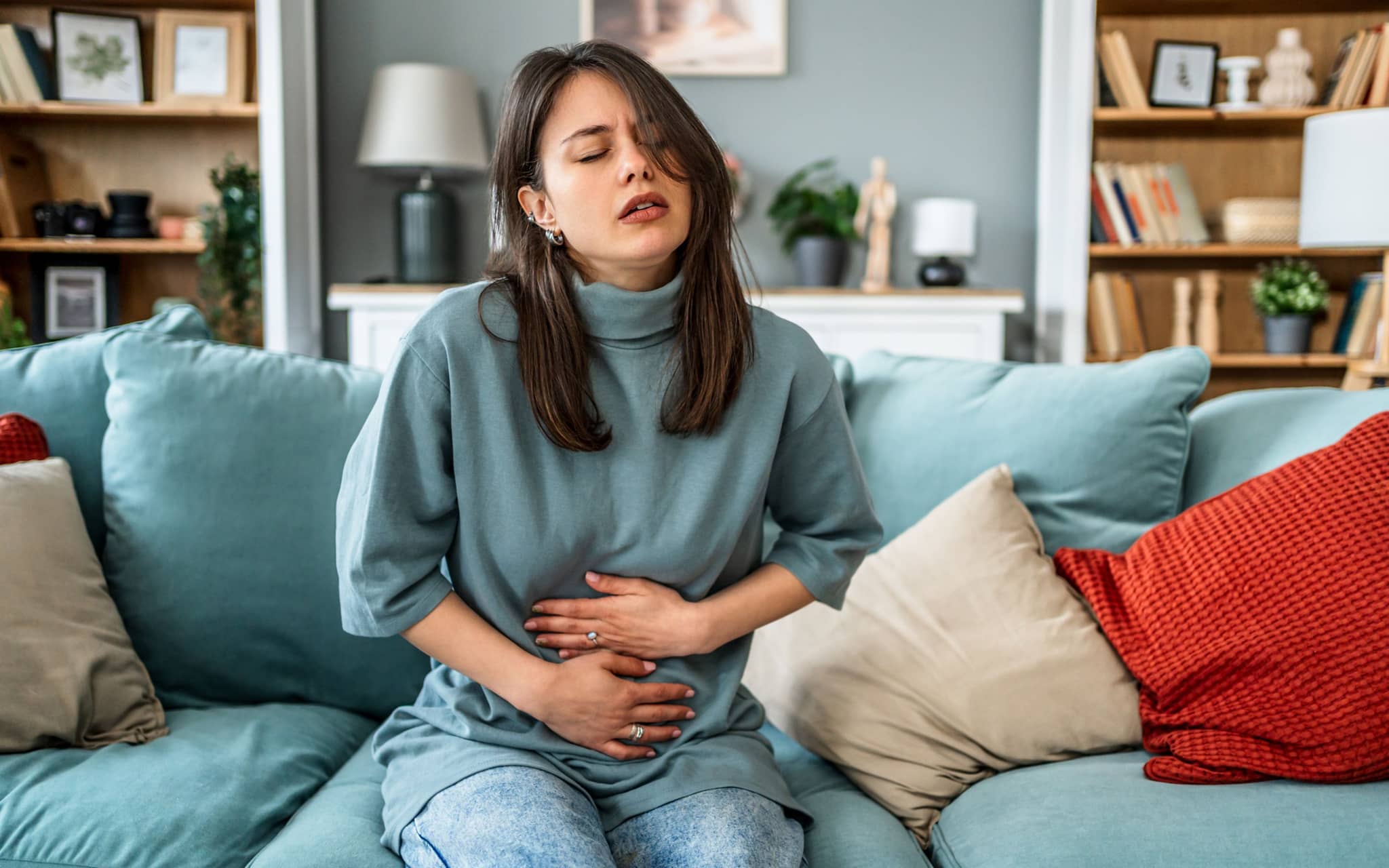 Blähungen während der Periode: Eine Frau sitzt auf einem Sofa und hält sich den Bauch fest