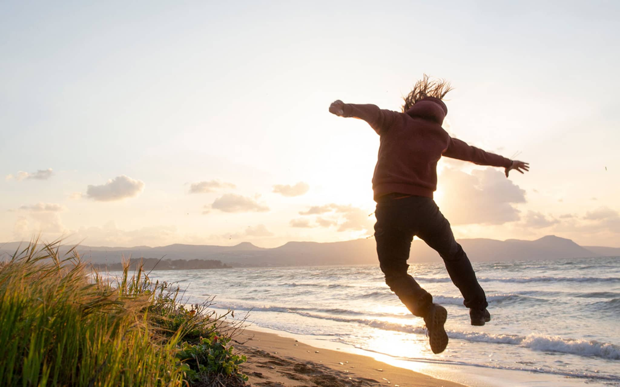 Ein Mann springt am Strand hoch und zeigt, dass er fit und vital ist.