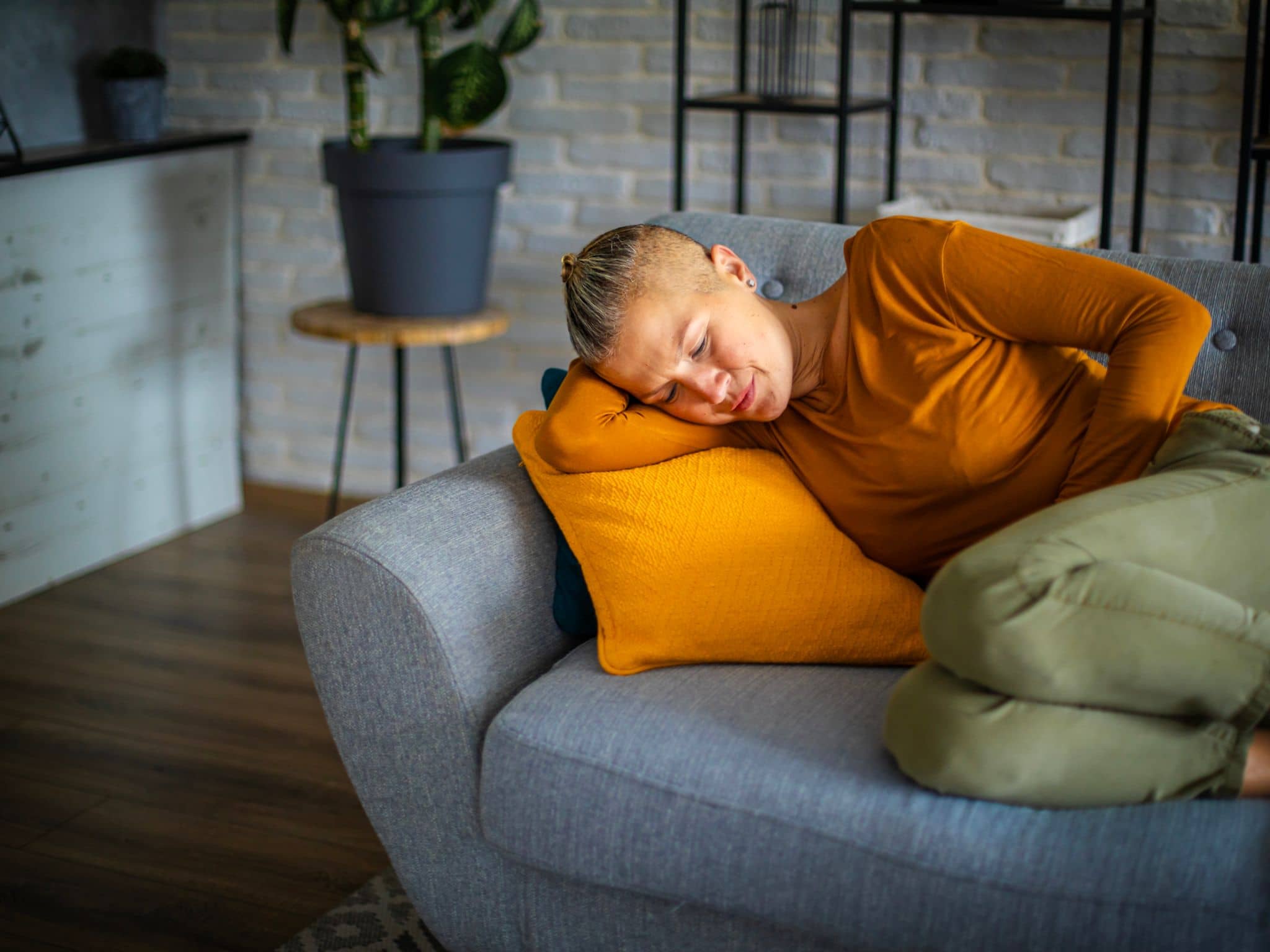 Durchfall bei der Periode: Eine Frau liegt auf dem Sofa und hält ihre Hand schützend vor den Bauch